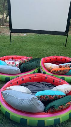 three inflatable beds sitting on top of grass near a movie projector screen