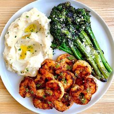 a white plate topped with shrimp, mashed potatoes and asparagus next to broccoli