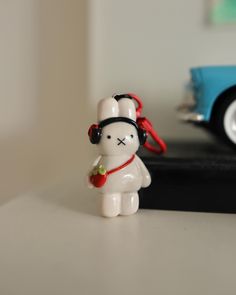 a white toy with a red ribbon around it's neck is standing next to a blue car