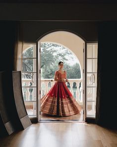 a woman standing in front of an open door wearing a red and gold dress with intricate patterns