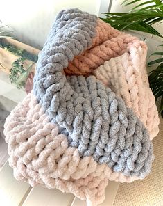 three different colored blankets sitting on top of a wooden table next to a potted plant