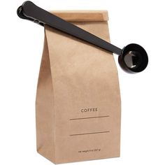 a paper bag with a black spoon in it next to a coffee bag on a white background