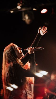 a woman with long hair holding her hands up in the air while singing into a microphone