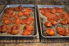 two metal trays filled with cooked meat on top of a counter