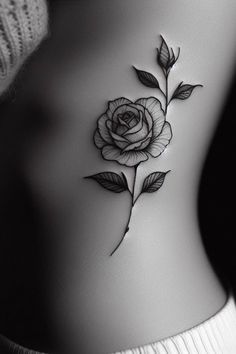 a black and white photo of a rose tattoo on the side of a woman's stomach