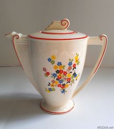 a white tea pot with colorful flowers painted on it's side and red trim around the top