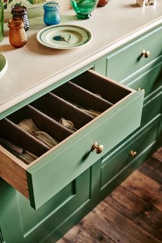 an open drawer in the middle of a kitchen counter with plates and glasses on it