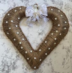 a heart shaped wreath with white flowers and pearls on the front is hung on a marble wall