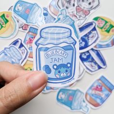 someone holding up a blueberry jam sticker in front of many other stickers