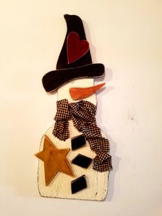 a wooden snowman with a hat and scarf on it's head, standing against a white wall