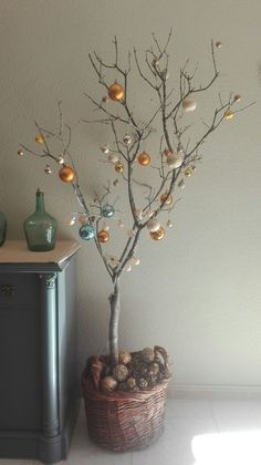 a potted tree with ornaments on it in front of a wall and a cabinet