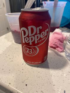 a can of dr pepper sits on a counter top next to plastic cups and water bottles