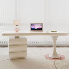 a laptop computer sitting on top of a white table next to a vase and lamp