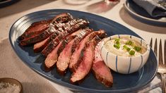 a blue plate topped with steak and mashed potatoes next to a bowl of sauce