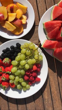 two white plates filled with fruit on top of a wooden table next to watermelon slices