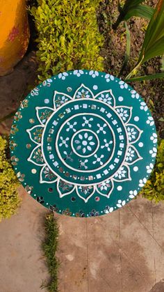 a blue and white painted plate sitting on top of a cement walkway next to green plants