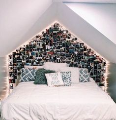 a white bed topped with lots of pictures under a slanted ceiling next to a window