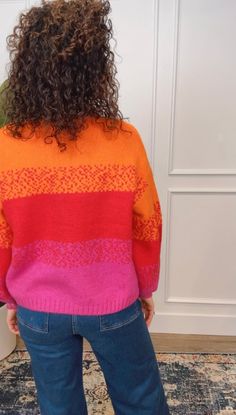 a woman with curly hair standing in front of a door wearing an orange and pink sweater