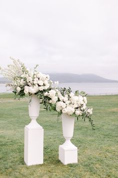 two white vases with flowers are on the grass