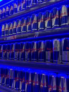 several rows of soda cans are lit up in blue lights and stacked on top of each other