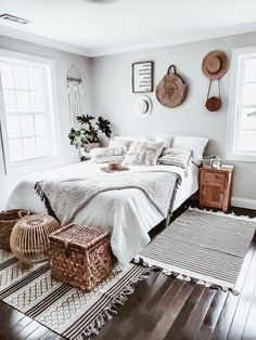 a bedroom with white walls and wood flooring is pictured in this image, there are wicker baskets on the bed