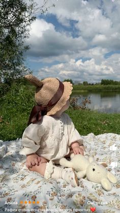 a baby sitting on a blanket with a stuffed animal in it's lap looking at the water