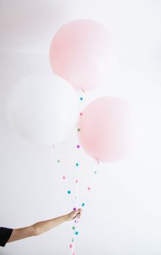 a person holding three balloons in the air with confetti on them and streamers