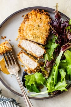 a white plate topped with meat and salad next to a fork on top of a table