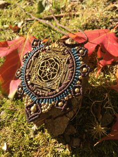 a beaded necklace sitting on top of a rock in the grass next to leaves