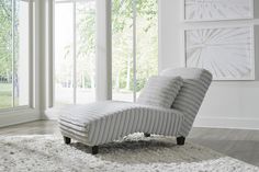 a white chaise lounge chair sitting on top of a shaggy rug in front of large windows