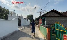 a man walking down a street next to a white fence