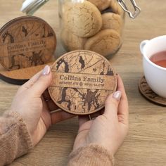 a person holding up a coaster next to a cup of tea and cookies on a table