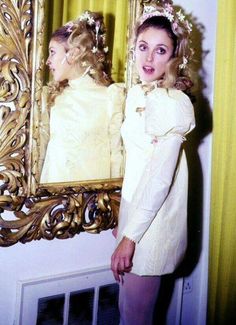 a woman standing in front of a mirror wearing a dress and headpiece with flowers on it