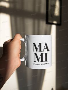 a person holding a coffee mug with the words mami on it in black and white