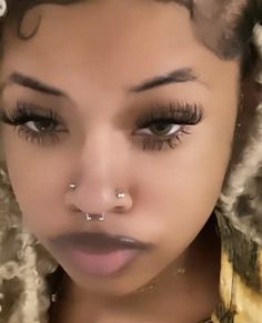 a close up of a woman with fake eyelashes and piercings on her nose, looking at the camera