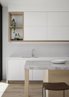 a modern kitchen with white cabinets and marble counter tops, along with a wooden dining table