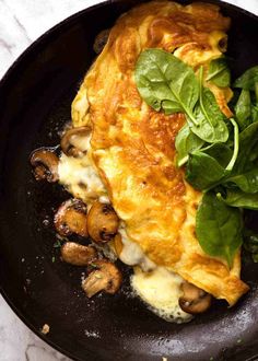 an omelet with spinach leaves and mushrooms in a skillet on a marble table