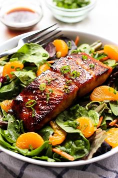 a salad with salmon, oranges and greens in a white bowl on a table