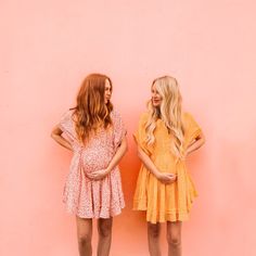 two young women standing next to each other in front of a pink wall with their hands on their hips