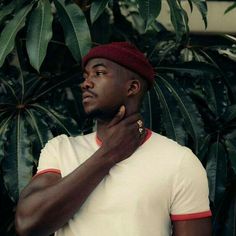 a man in a white shirt and red hat standing next to a tree with green leaves