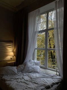 an unmade bed in front of a large window with sheer curtains on the sides