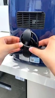 two hands are holding an object in front of a blue device that is on top of a table