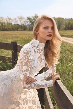 a woman leaning on a fence wearing a white dress with floral appliques and long sleeves