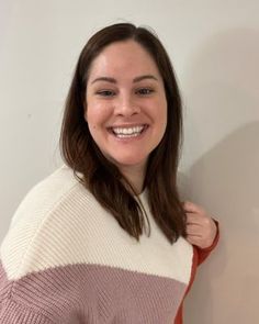 a woman is smiling and wearing a pink and white sweater with an orange stripe on it