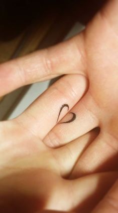 a person's hand with a tiny heart tattoo on it, holding the finger of another person