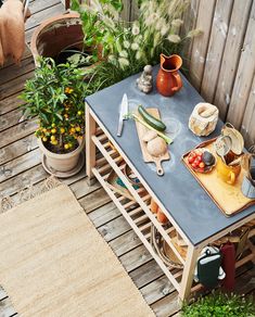 an outdoor table with potted plants and cutting boards on it in the middle of a wooden deck