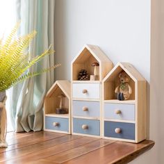 two wooden toy houses sitting on top of a table next to a potted plant