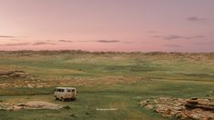 an old van is parked in the middle of a grassy field with rocks and grass