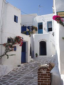 an alley way with white buildings and flowers growing on the windows, doors and shutters