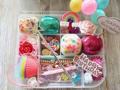 a plastic container filled with lots of different types of candies and balloons on top of a wooden table